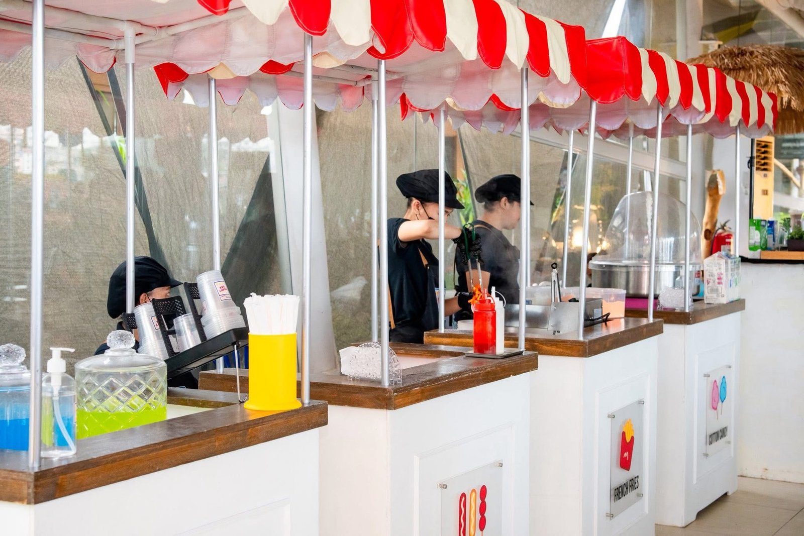 PartyBox crew serving drinks, hotdogs, fries and cotton candy from a row of striped-awning carts